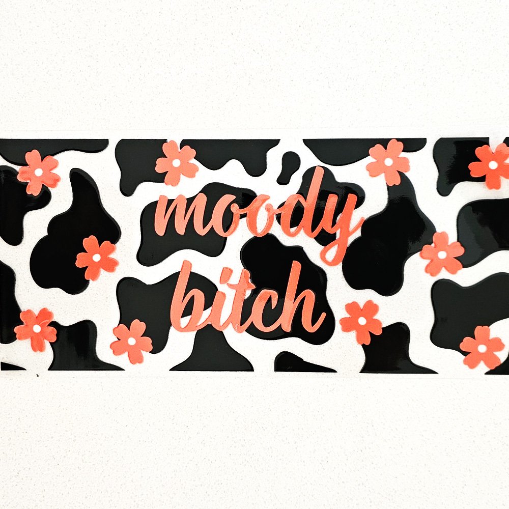 Vinyl decal with black cow print background, coral flowers, and the phrase "moody bitch" in cursive font.