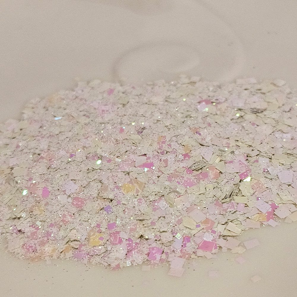 Pastel iridescent flake glitter in pink, white, and gold tones on a soft beige background